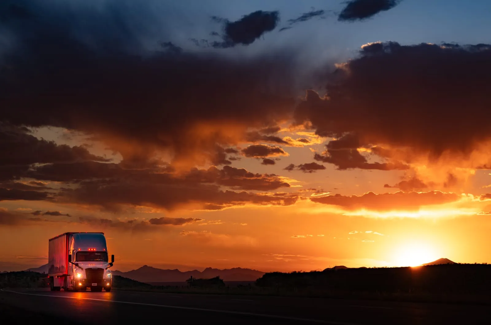 Semi Truck With Headlights On Under a Fiery Sunset