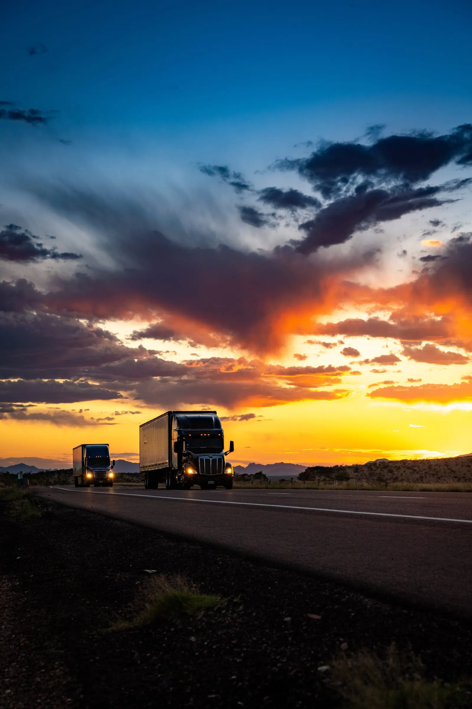 Semi Trucks Under Orange Storm Clouds at Sunset